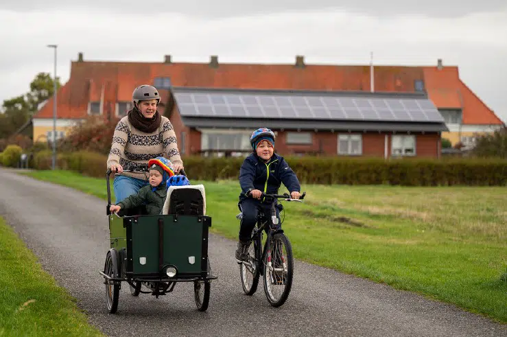 Foto af kvinde på ladcykel med søn cyklende ved siden af.