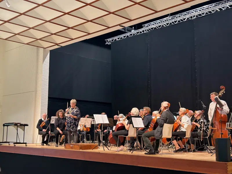 Borgmester Trine Græse holder tale på en scene i det nyrenoverede lokale med et stort orkester bag sig.  