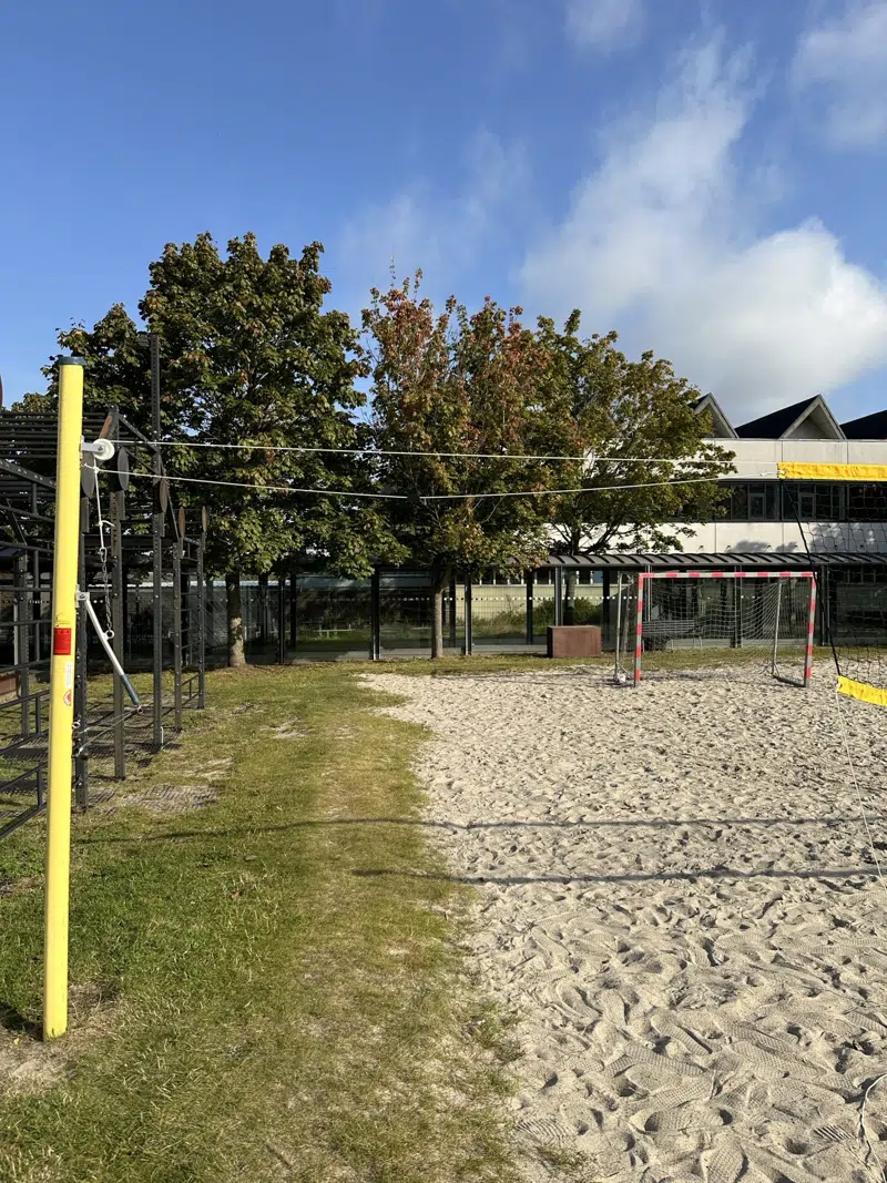 Træk håndtaget ned og fastgør det, så nettet strammes helt op. Fastgør derefter den næstøverste snor i den øverste krog på den gule stolpe, og dernæst den næstøverste snor på den anden stolpe, som strammes godt op.