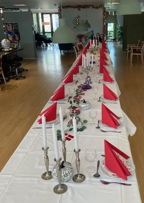 Et flot opdækket langbord med hvid dug, røde servietter og lysestager