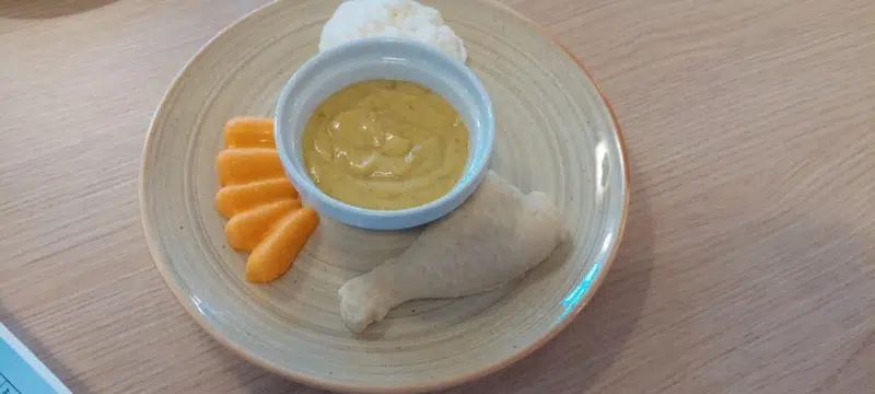 En rund tallerken med blød og synkevenlig mad og en lille rund skål med dip/sauce