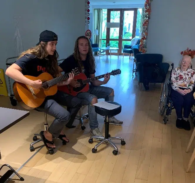 To elever fra engdomsskole spiller på guitar. Ude i højre side af billedet, sidder en beboer fra Egegåden i kørestol