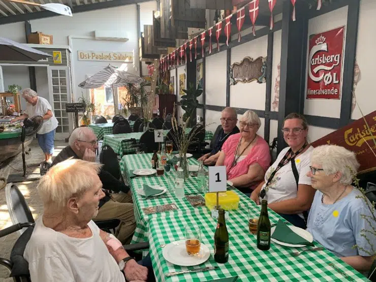 En flok beboere fra Egegården og en medarbejder spiser frokost ved et langbord med grønternet dug