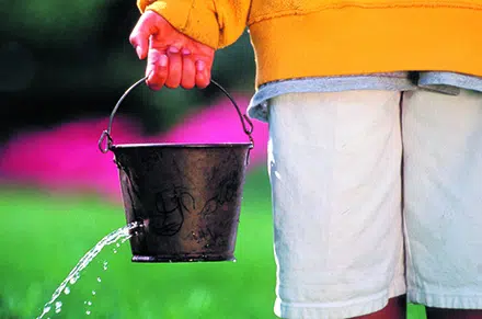 Barn holder en spand med hul i, hvor der løber vand ud