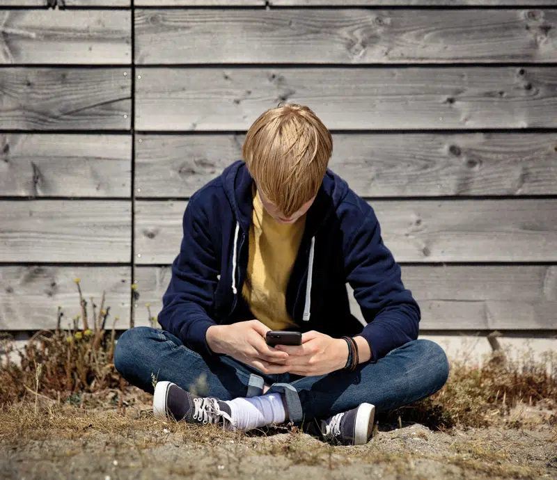 Ung mand sidder med hovedet bøjet og mobilen i hænderne