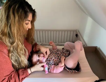 Barn der ligger på puslebord og er ved at få børstet tænder. 