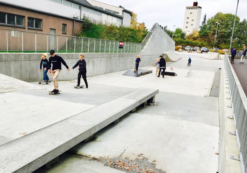 Skaterbane i beton med små og større børn på løbehjul og skateboard