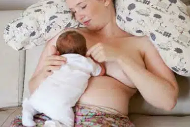 Tilbagelænet ammestilling, hvor mor sidder tilbalænet og støttet af puder i ryggen. Barnet ligge på maven mod mors mave.