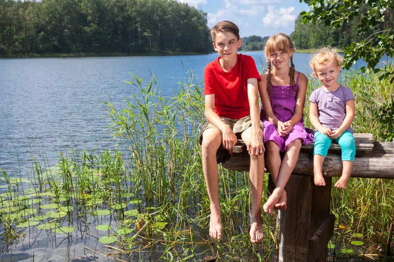 Tre børn sidder ved en sø