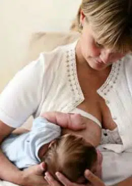 Tvillingestilling, hvor mor sidder op, og barnets krop og ben ligger bagud under mors arm. Mor støtter barnets hoved i sin hånd