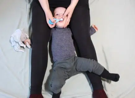 Barn der ligger mellem benene på voksen og får børstet tænder