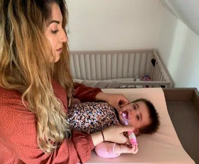 Barn der ligger på et puslebord og får børstet tænder af en voksen