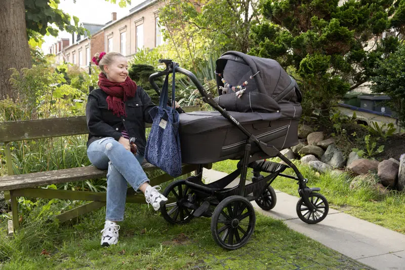 Ung kvinde sidder på bænk ved en barnevogn