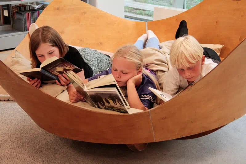 Børn ligger på vippe-møbel og læser