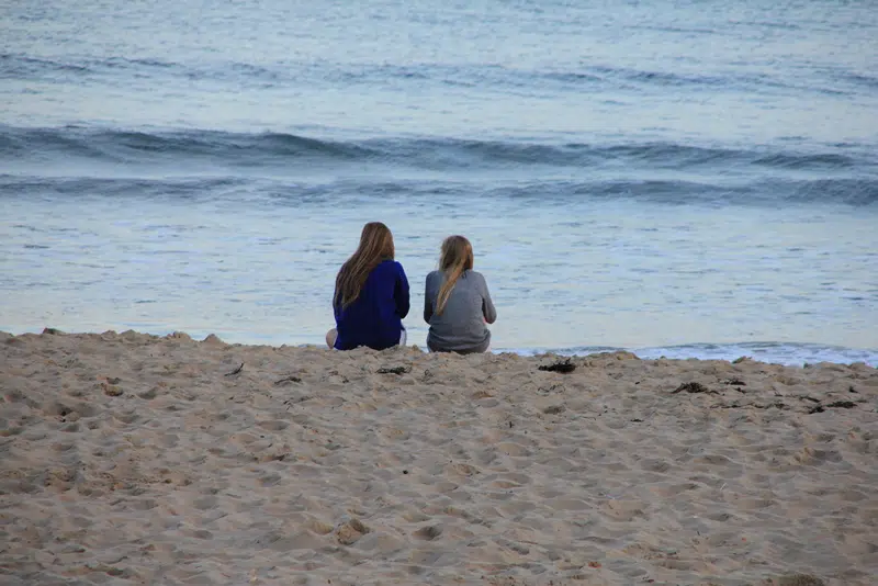 To piger der sidder på stranden og kigger ud over vandet