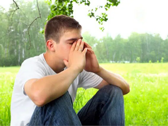 En mand, der sidder i et græsareal med hænderne på ansigtet