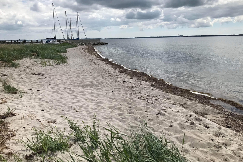 Foto af strandbred med bådemaster i baggrunden