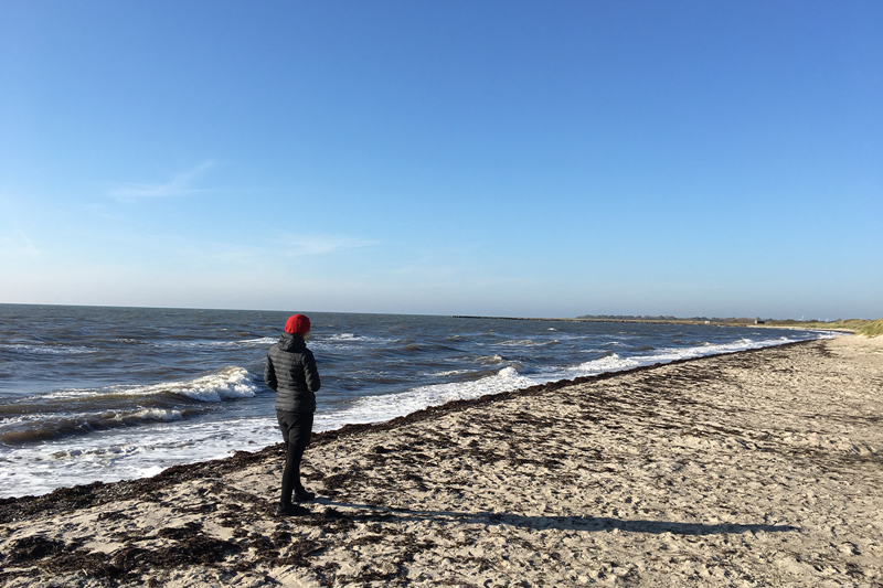 Foto af person der går langs strandbreden der er lidt skumtoppe på bølgerne