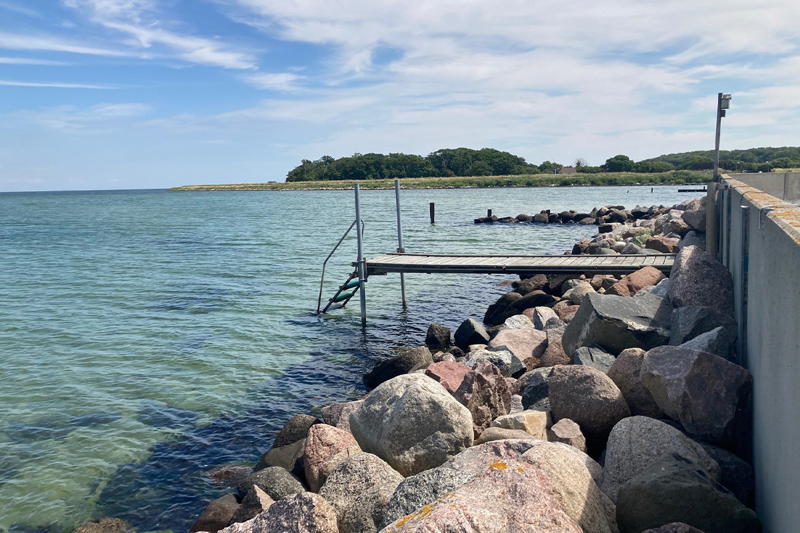 foto af badebro tæt på havnekaj og stenmole med skov i baggrunden